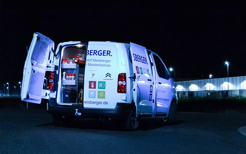 Ein weißer Handwerker-Transporter steht nachts auf einem Parkplatz, beleuchtet von Straßenlaternen im Hintergrund.
Die Hecktüren des Fahrzeugs sind geöffnet, sodass die voll ausgestattete mobile Werkstatt im Inneren sichtbar ist – mit Regalen, Werkzeugen und Materialien. Auf der Außenseite des Fahrzeugs sind das Logo „Meisberger“ sowie Piktogramme zu Heizung, Wärmepumpe, Bad & Sanitär, Solar- & Umwelttechnik abgebildet. Der Transporter ist ein Citroën-Firmenfahrzeug.