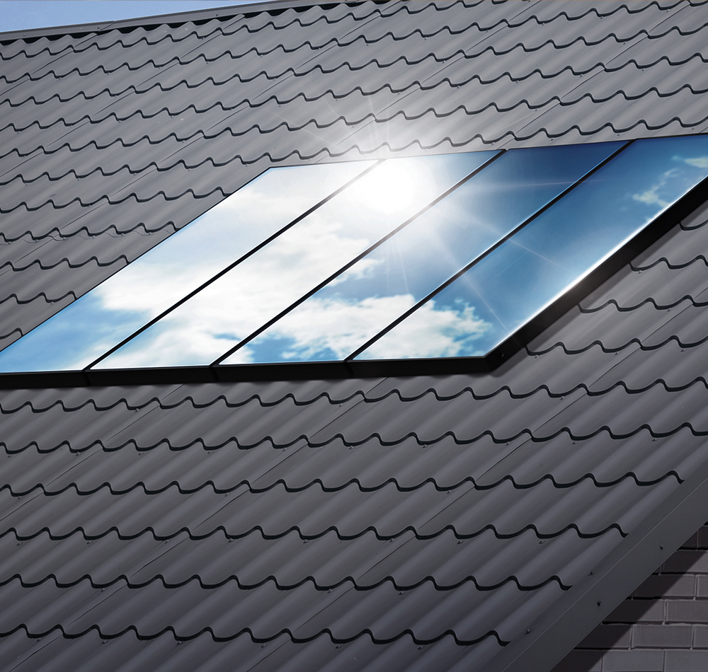Ein graues Dach eines Wohnhauses, auf dem mehrere Solarpanels montiert sind. Die glänzenden Oberflächen der Module spiegeln den blauen Himmel, während direktes Sonnenlicht darauf fällt.